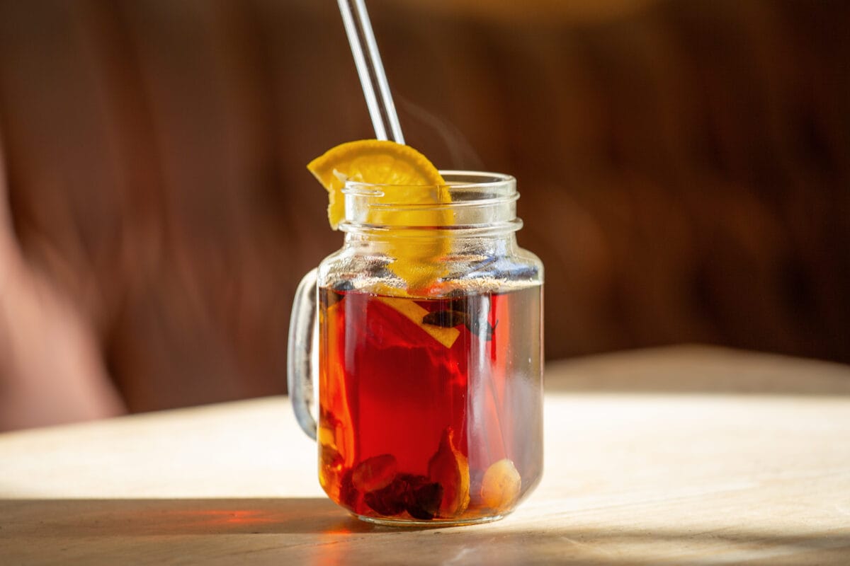 Cascara punsch mit orange garniert in glas auf einem holztisch von der sonne angestrahlt