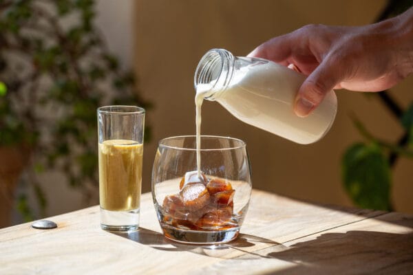 Pistazien Spanish Latte in der Zubereitung - aufgeschäumte Milch wird in das Glas mit Kaffee-Eiswürfeln eingegossen