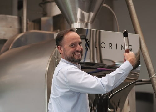 lachender Mann an einem Kaffeeroester, haelt Hebel in der Hand